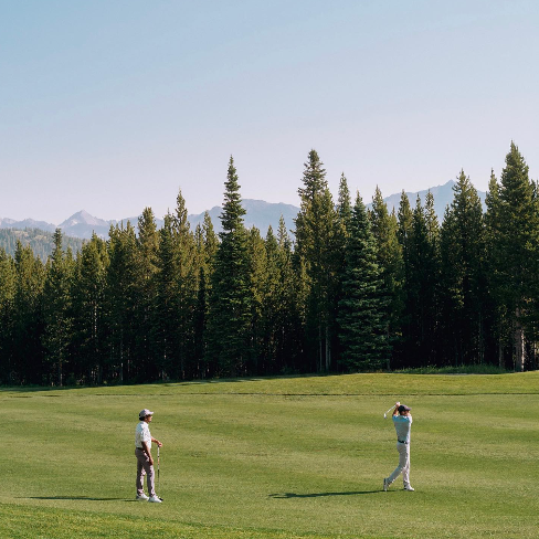 Two men on a golf course with mountains in the background